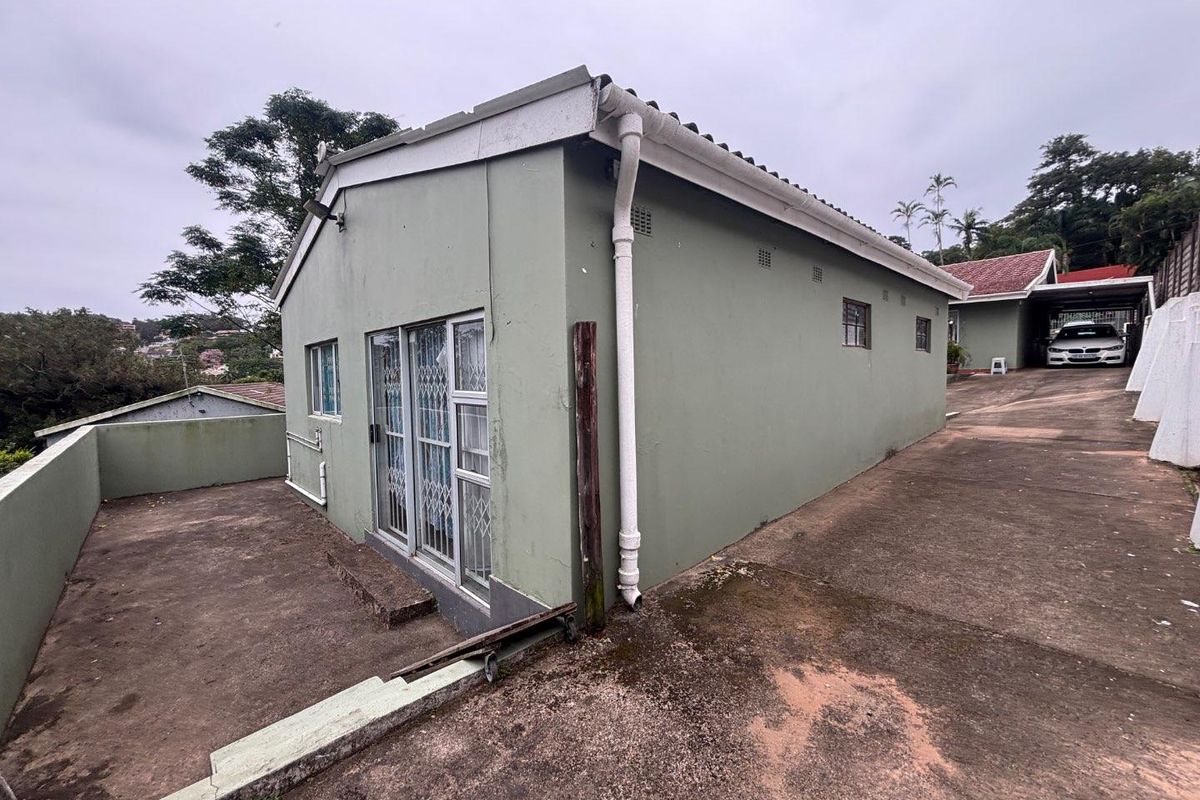 Exterior view of the property showing the side facade, concrete driveway, and paved area with security gates on the sliding doors.