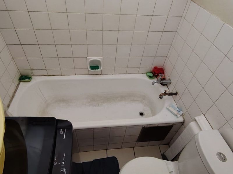 A compact bathroom featuring a standard bathtub with tiled surround and a toilet, requiring cosmetic updates and fixture maintenance.