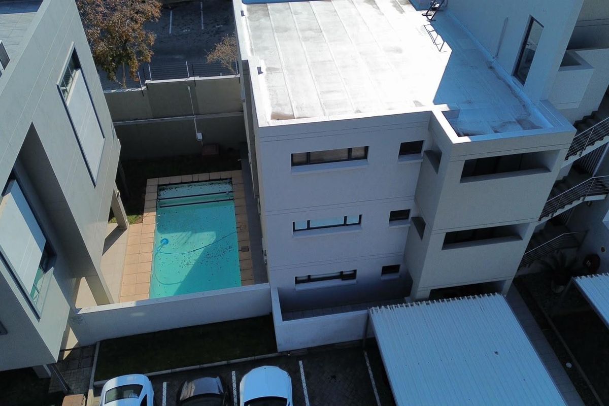 Aerial view of the apartment complex featuring a swimming pool, paved parking area, and covered carports.