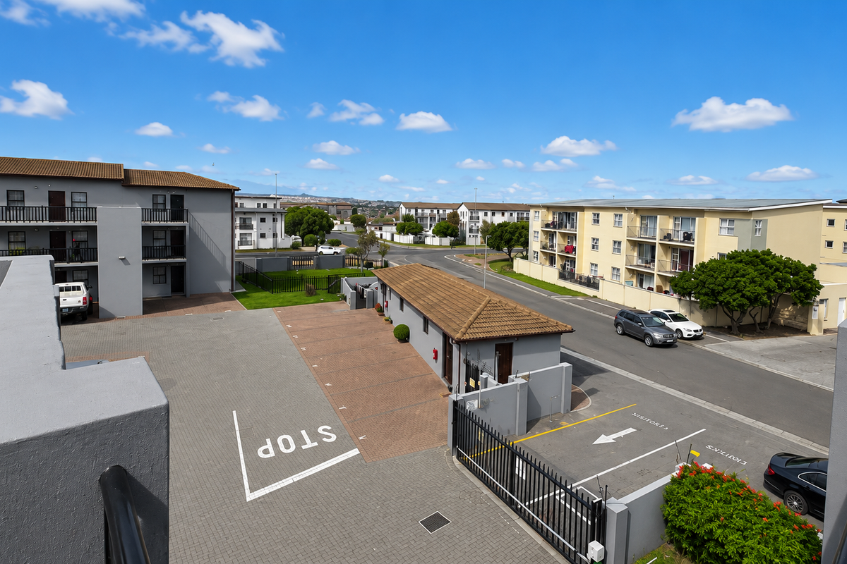 An elevated aerial view of the apartment complex grounds, featuring paved parking areas, security access gates, and surrounding residential buildings.