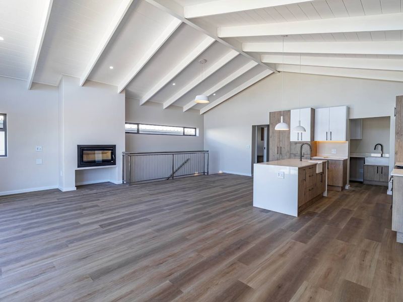 Spacious open-plan living area featuring a vaulted ceiling with exposed beams, modern kitchen with island, and a built-in fireplace, finished with high-quality laminate flooring.