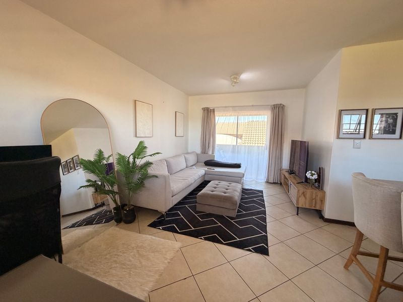 A bright and well-maintained living room featuring neutral tiled flooring and a sliding glass door that provides access to the outdoor area.