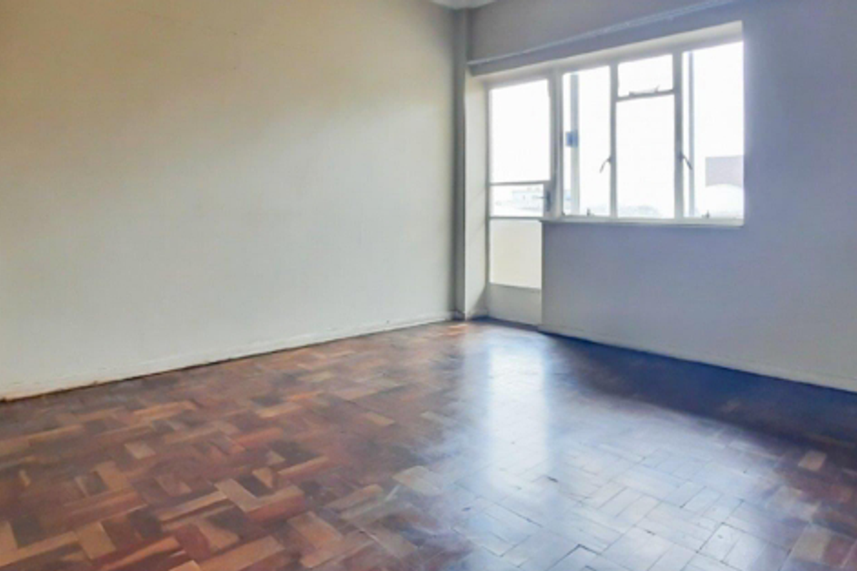 An empty living room featuring original parquet flooring, large windows, and a glass-paneled door leading to an outdoor area.