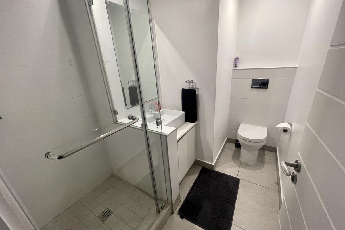 Modern bathroom featuring a glass-enclosed shower, wall-mounted toilet, and a sleek vanity basin with clean tiled finishes.