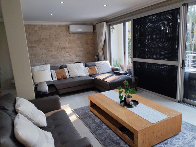 A well-maintained living room featuring a stone accent wall, recessed lighting, split-system air conditioning, and large sliding glass doors leading to an outdoor area.