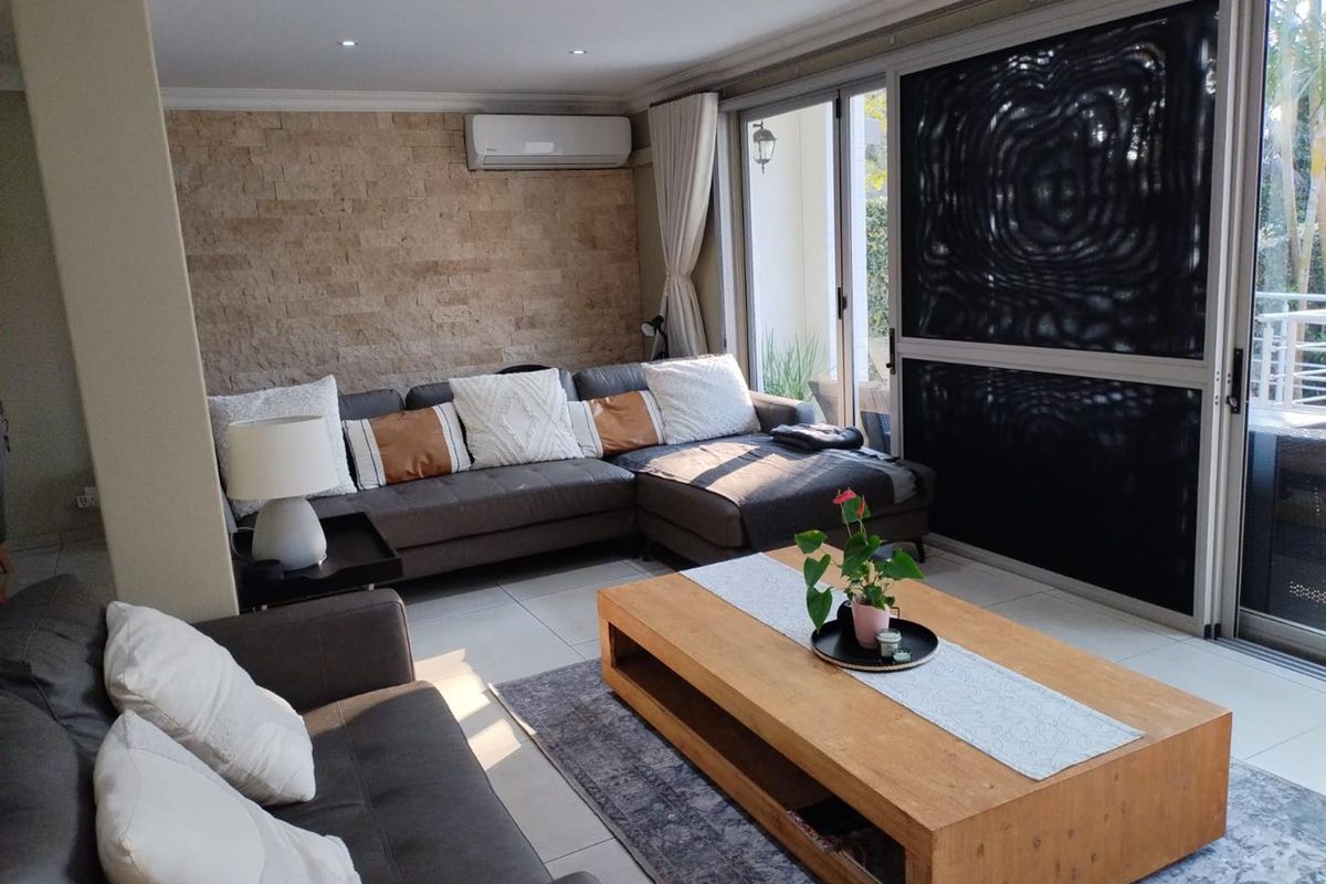 A well-maintained living room featuring a stone accent wall, recessed lighting, split-system air conditioning, and large sliding glass doors leading to an outdoor area.