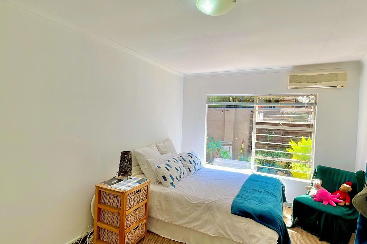 A functional bedroom featuring a louvered window, split-system air conditioning unit, and neutral finishes, offering a comfortable and well-lit living space.