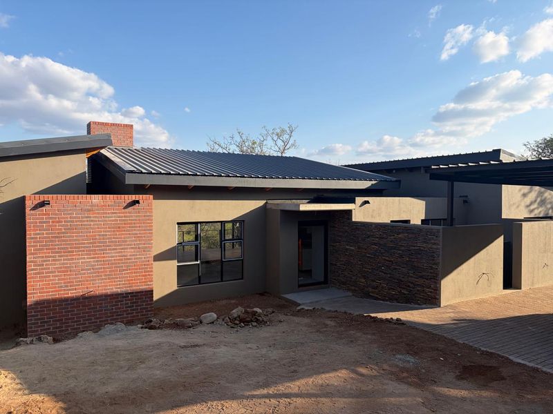 Modern single-story home featuring a combination of face brick, stone cladding, and corrugated metal roofing with an unfinished front garden area.