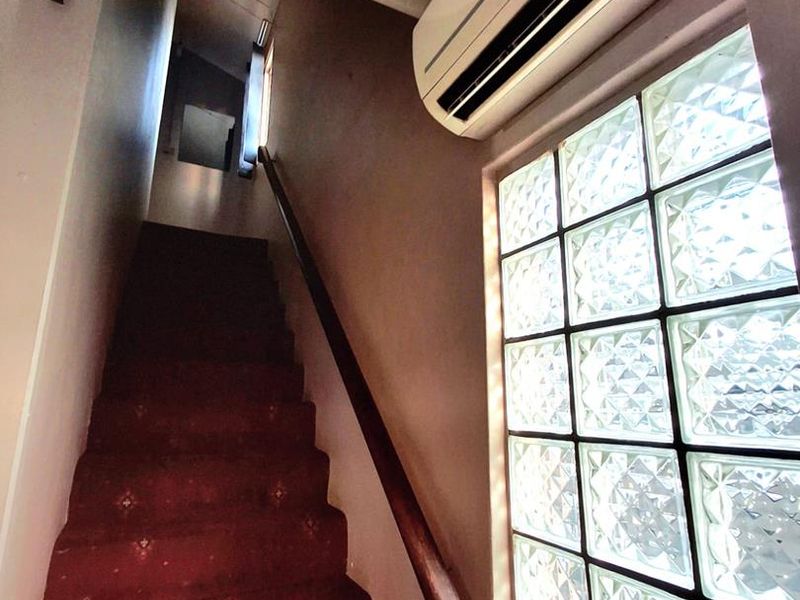 A staircase hallway featuring a glass block window, timber handrail, and wall-mounted air conditioning unit.