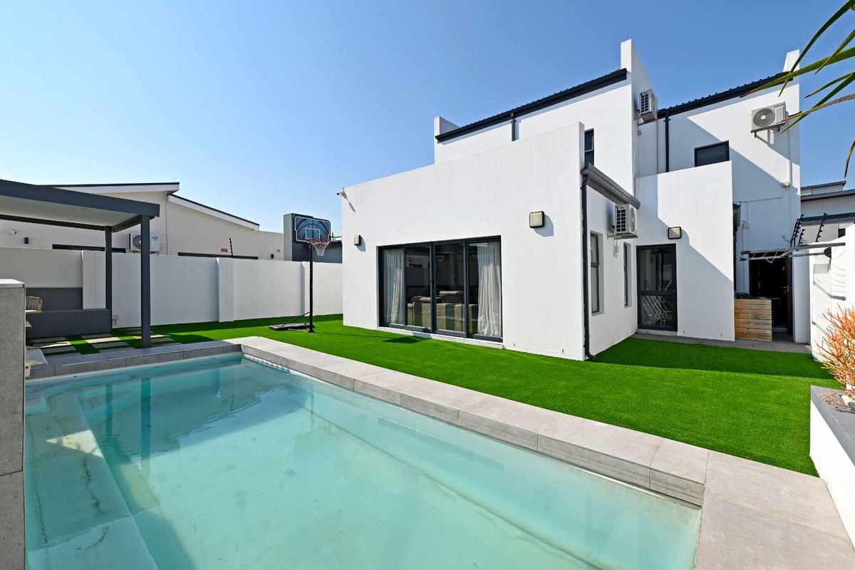Rear exterior view featuring a swimming pool, artificial lawn, and modern white facade with sliding glass doors and integrated air conditioning units.