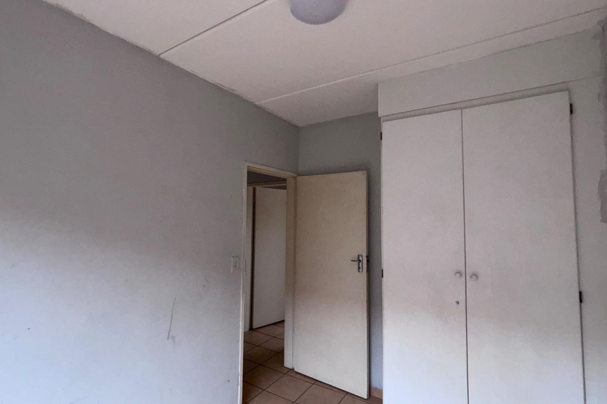 An empty bedroom featuring built-in wardrobes, tiled flooring, and neutral wall finishes, offering a blank canvas for potential updates or staging.