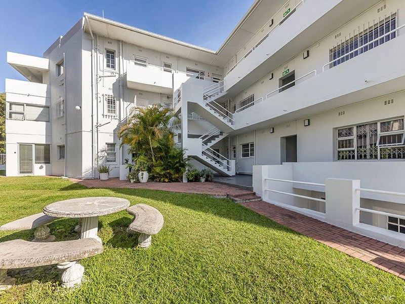 Rear view of the apartment complex featuring a communal garden, paved walkways, and external staircases providing access to upper-level units.
