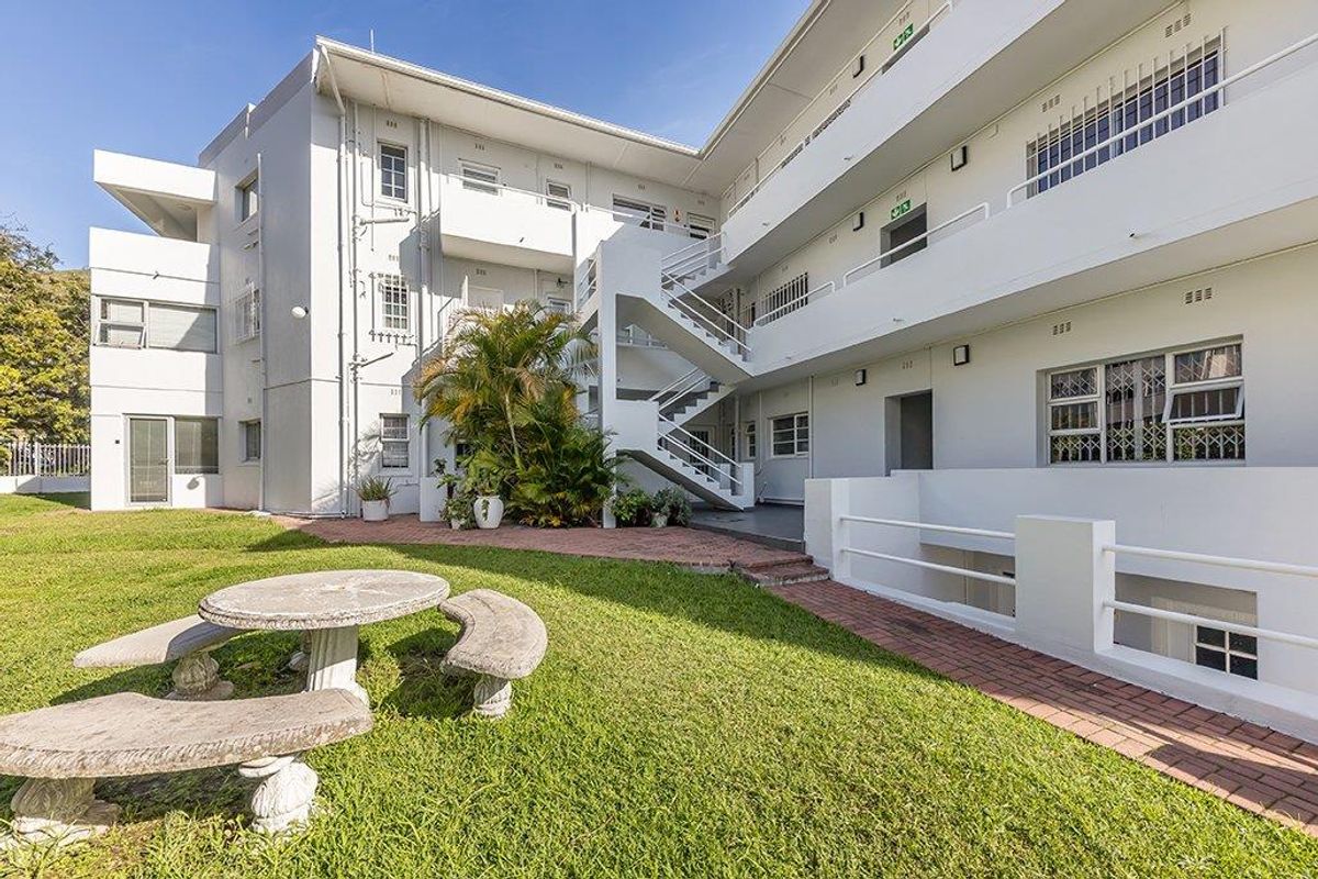 Rear view of the apartment complex featuring a communal garden, paved walkways, and external staircases providing access to upper-level units.