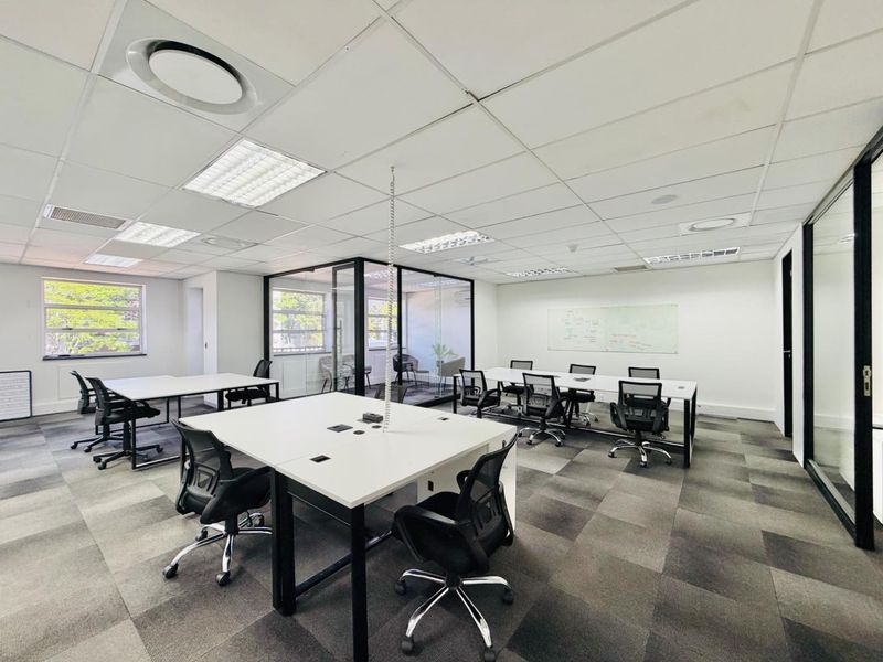 A modern, open-plan office space featuring glass partitions, suspended ceilings with recessed lighting, and professional carpet tile flooring.