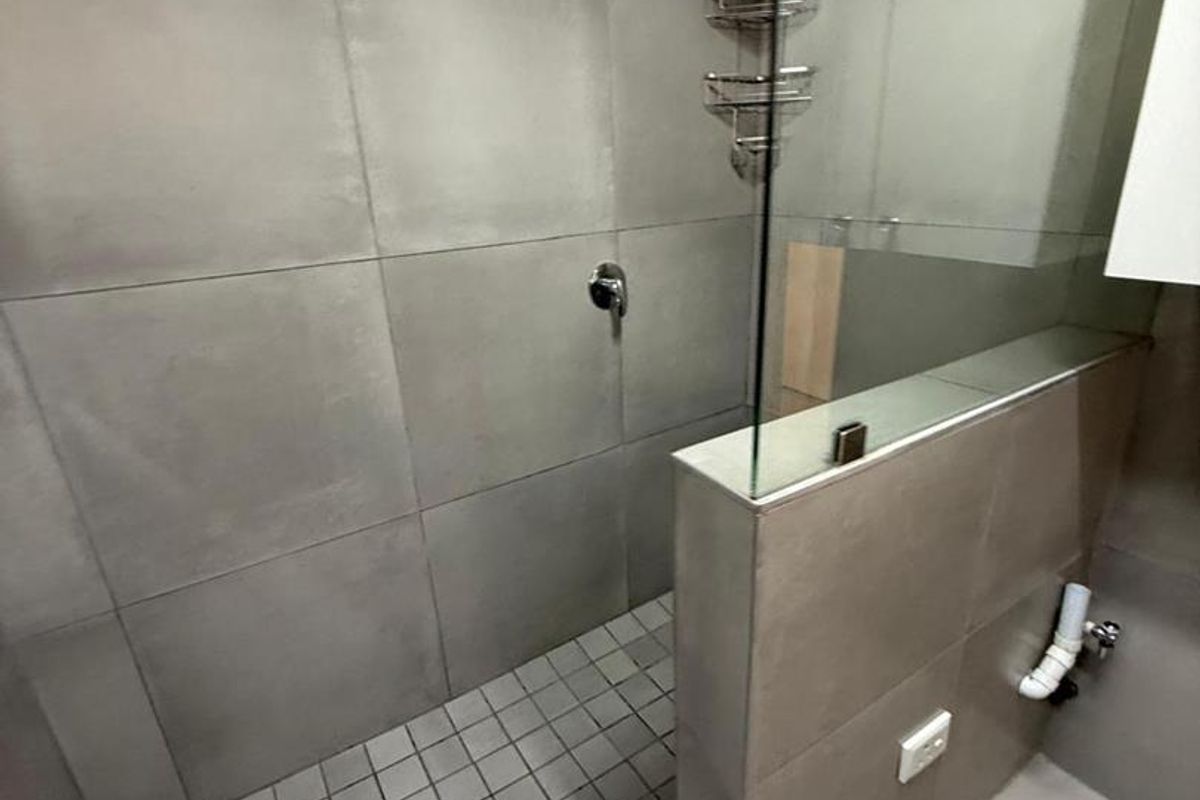Modern bathroom featuring a walk-in shower with large format grey tiles, a glass screen, and a rain shower head.