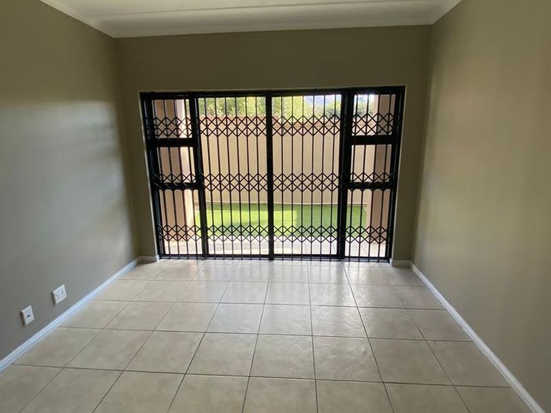 An empty living room featuring neutral wall paint, ceramic floor tiles, and a sliding glass door with a security gate leading to the outdoors.