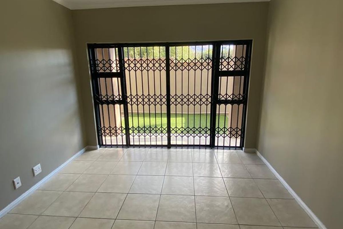 An empty living room featuring neutral wall paint, ceramic floor tiles, and a sliding glass door with a security gate leading to the outdoors.