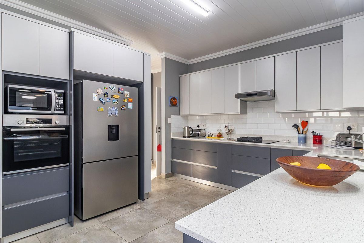 Modern kitchen featuring sleek grey and white cabinetry, quartz countertops, subway tile backsplash, and integrated appliances including an oven, microwave, and gas hob.