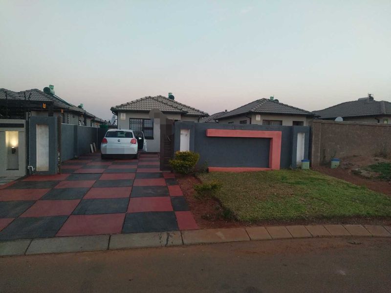 Front view of a residential property featuring a paved driveway with a checkered pattern, a boundary wall, and a tiled roof structure.