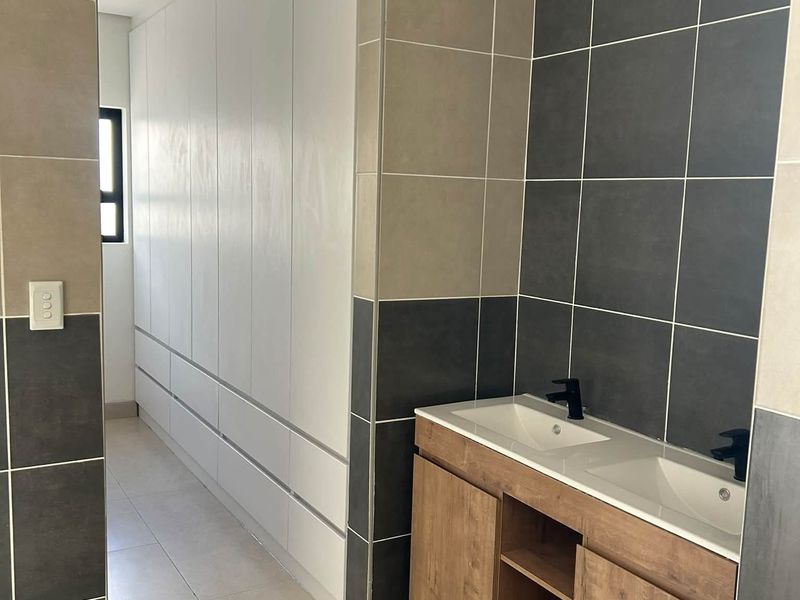 Modern bathroom featuring a double vanity with wood-finish cabinetry, black fixtures, and contemporary two-tone wall tiling with ample built-in storage.