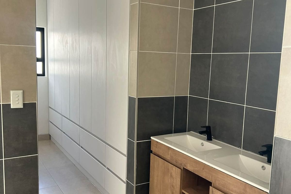 Modern bathroom featuring a double vanity with wood-finish cabinetry, black fixtures, and contemporary two-tone wall tiling with ample built-in storage.