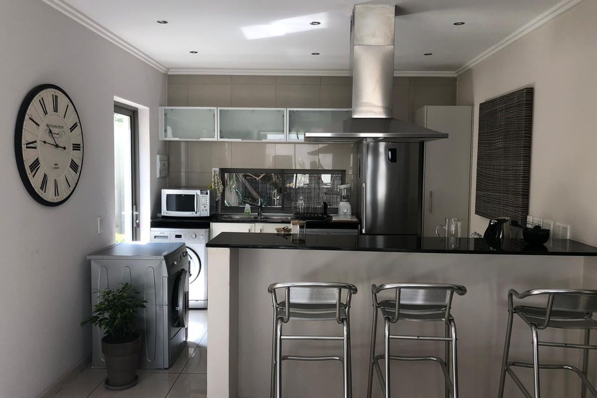 A functional kitchen featuring a granite breakfast bar, stainless steel extractor fan, tiled backsplash, and modern recessed lighting.