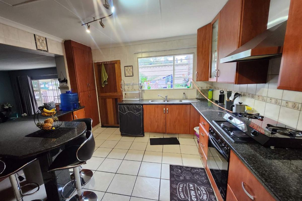 A functional kitchen featuring wooden cabinetry, granite countertops, a built-in oven with gas hob, extractor fan, and a breakfast nook area.