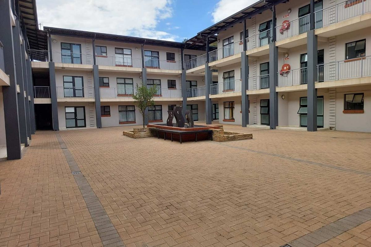 A paved central courtyard area within a multi-story townhouse complex, featuring a central water feature and access to surrounding residential units.