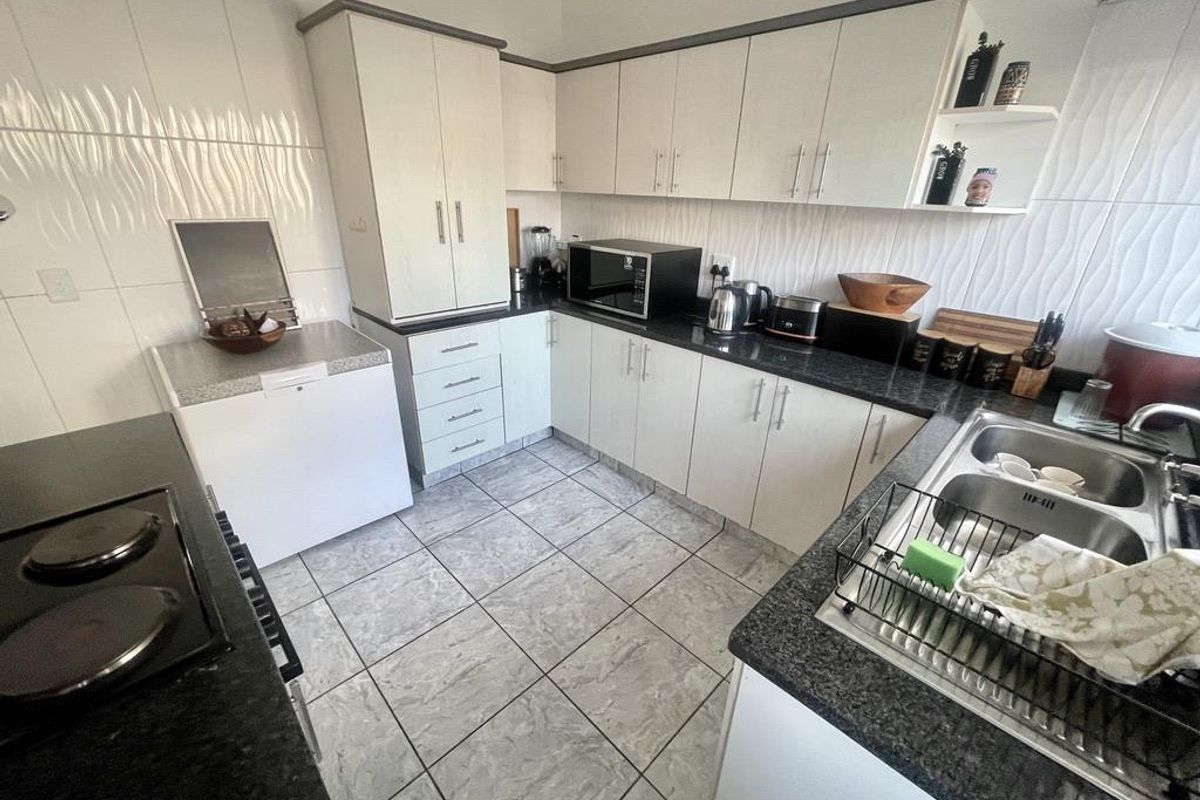 Functional kitchen featuring light-toned cabinetry, dark granite countertops, tiled flooring, and a double-basin stainless steel sink.