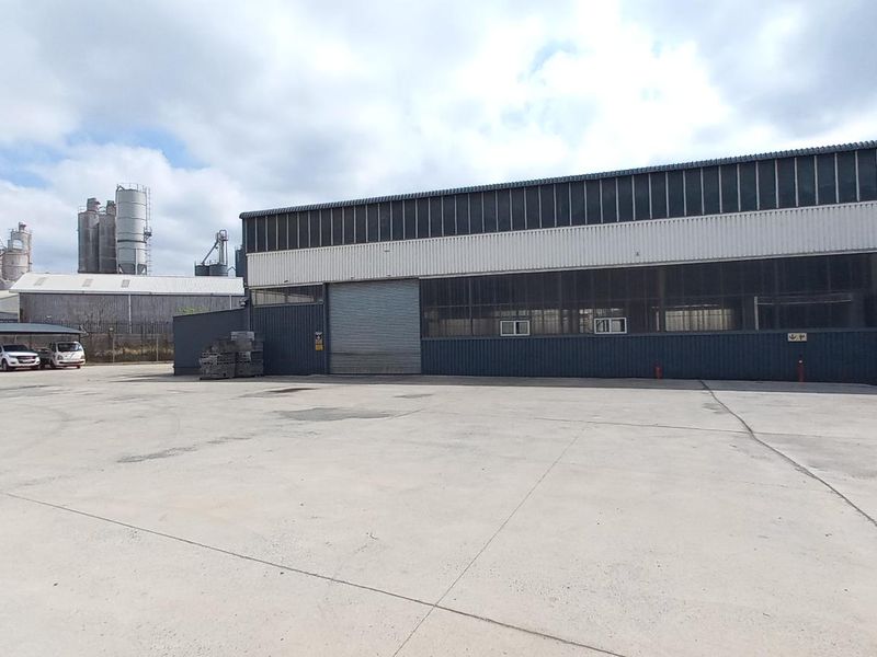 Industrial property exterior featuring a large concrete yard, metal cladding facade, and a roller shutter door entrance.