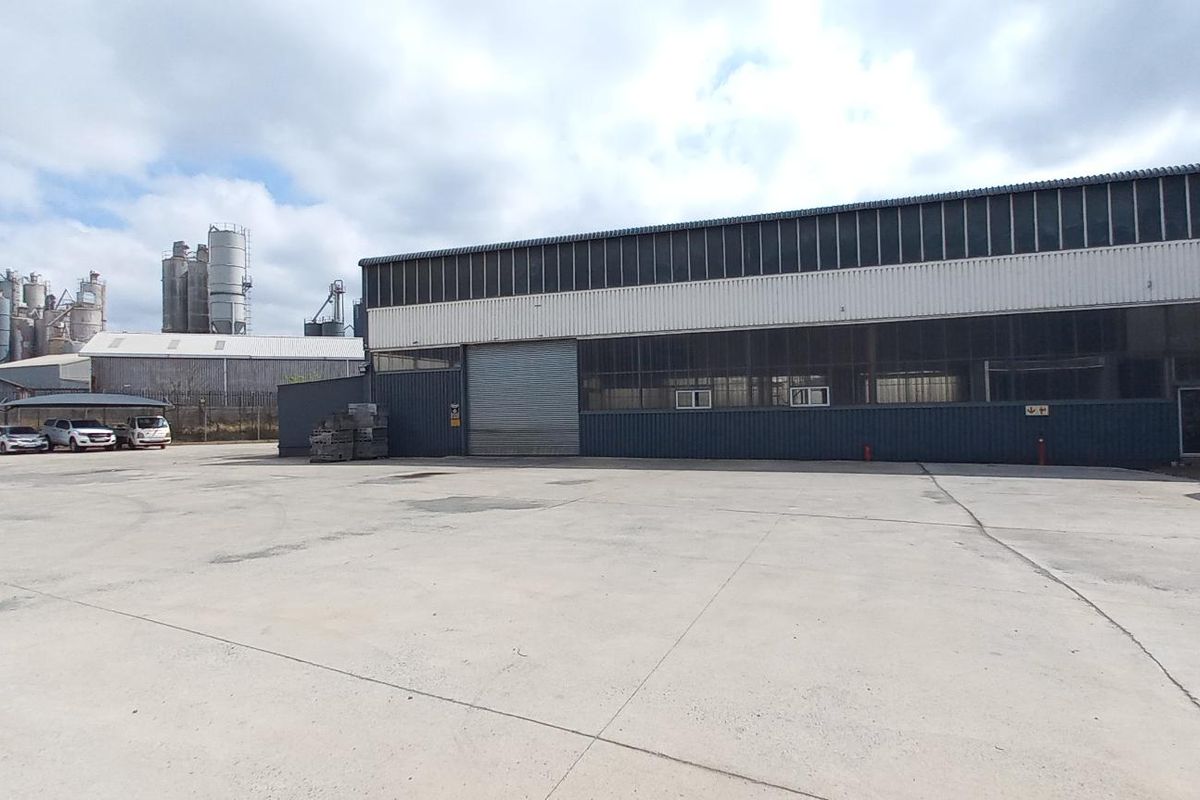 Industrial property exterior featuring a large concrete yard, metal cladding facade, and a roller shutter door entrance.