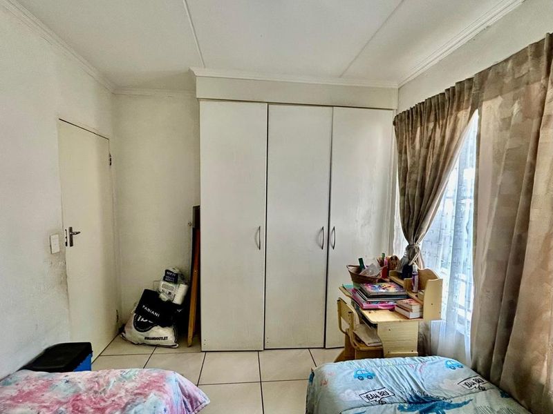 A bedroom featuring built-in cupboards, tiled flooring, and a window with curtains. The room requires minor cosmetic updates to the wall finishes.
