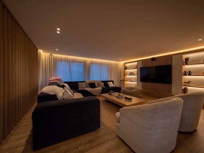 Modern living room featuring timber wall paneling, built-in shelving with integrated LED lighting, recessed ceiling lights, and high-quality laminate flooring.