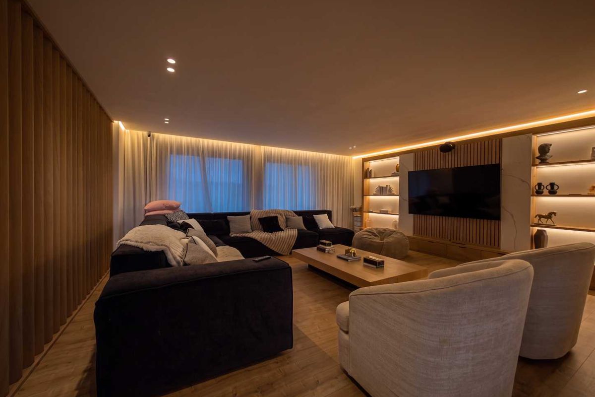 Modern living room featuring timber wall paneling, built-in shelving with integrated LED lighting, recessed ceiling lights, and high-quality laminate flooring.
