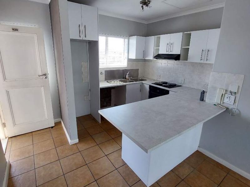 A functional kitchen featuring white built-in cabinetry, a breakfast bar, integrated oven and hob, and tiled flooring throughout.