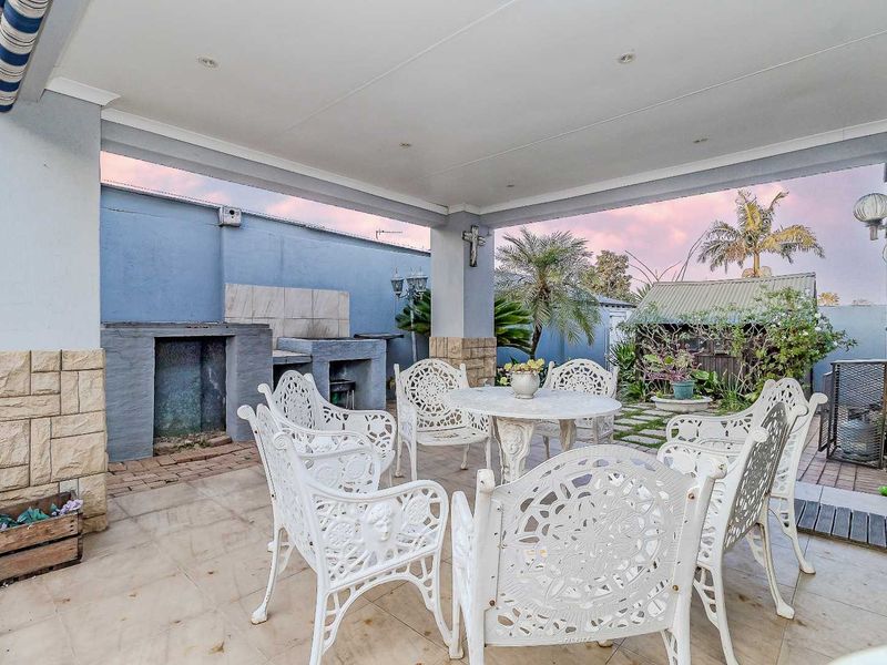 Covered patio area featuring a built-in braai, stone-clad pillars, and tiled flooring, providing a functional outdoor entertainment space.