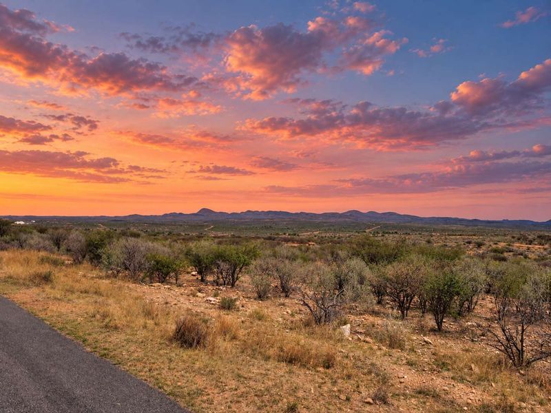 A scenic view of the expansive natural landscape and distant mountains at sunset, featuring a paved road in the foreground.