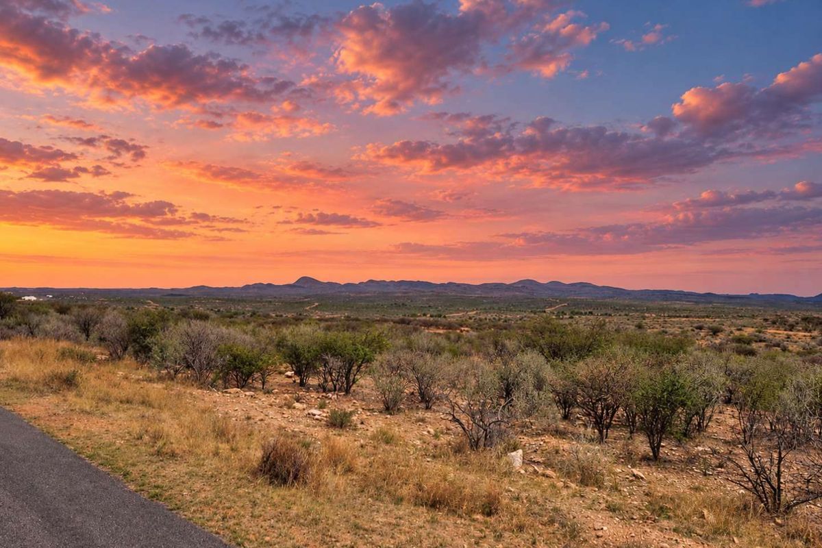 A scenic view of the expansive natural landscape and distant mountains at sunset, featuring a paved road in the foreground.