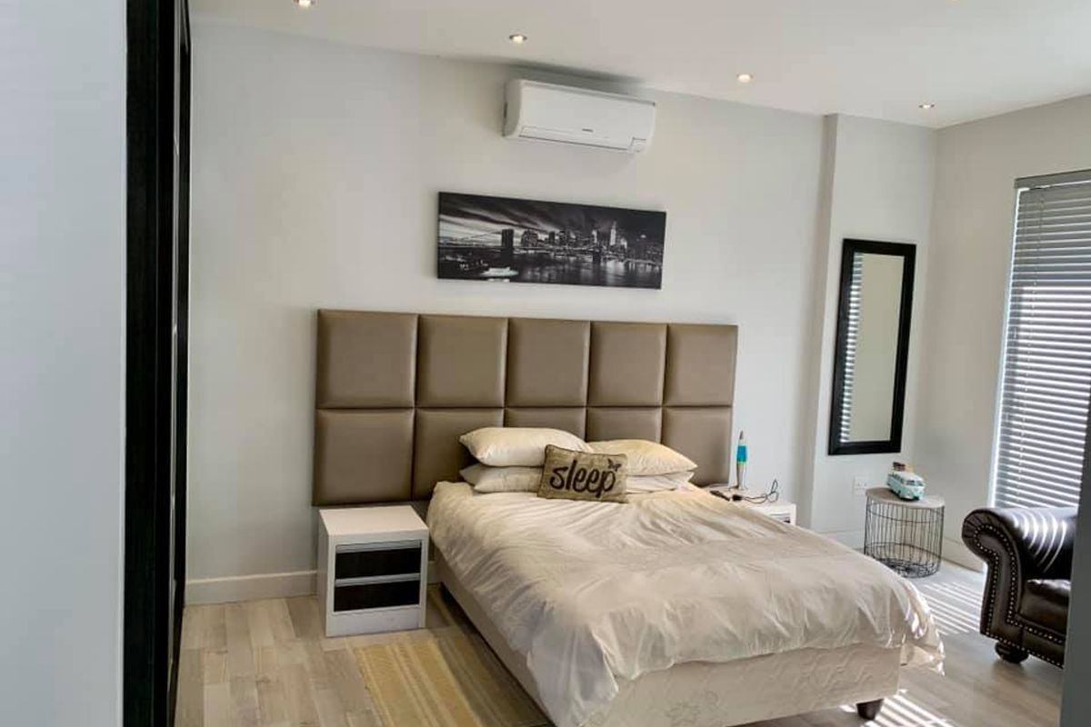 A well-maintained bedroom featuring recessed ceiling lighting, a wall-mounted air conditioning unit, and modern light-toned flooring.
