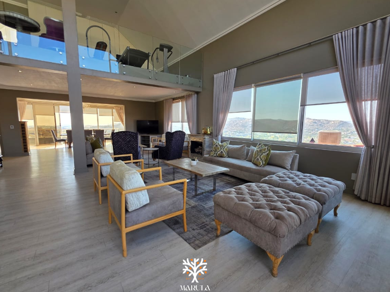 Spacious open-plan living area featuring a vaulted ceiling, mezzanine level with glass balustrade, fireplace, and expansive windows offering panoramic views.