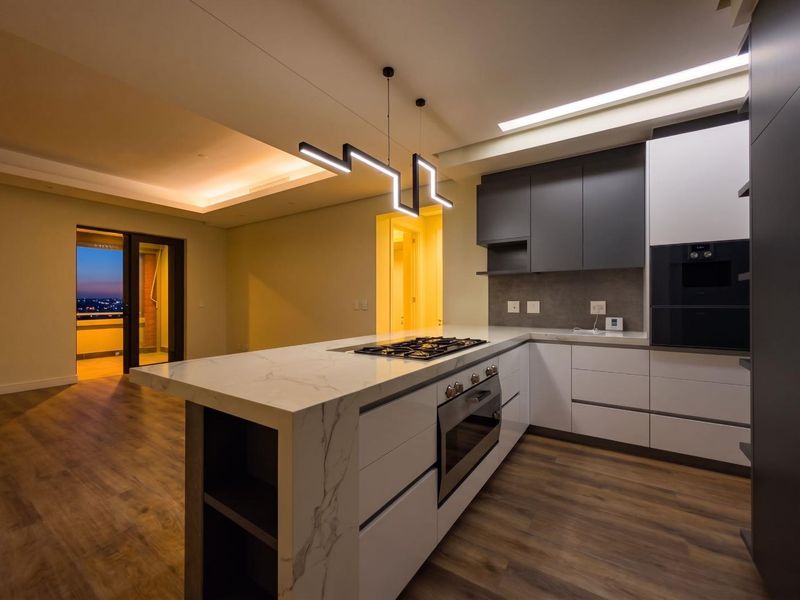 Modern kitchen featuring a marble-look stone island with integrated gas hob, built-in oven, sleek cabinetry, and contemporary pendant lighting in an open-plan layout.