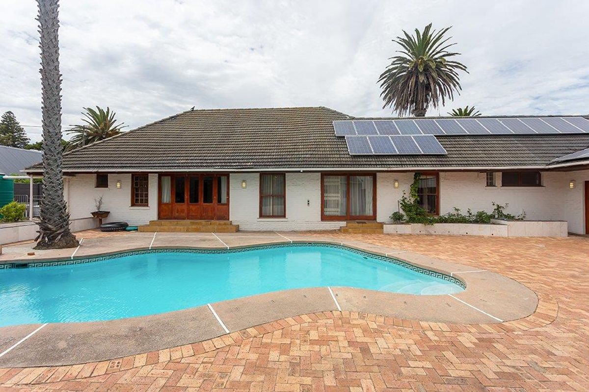 Rear exterior view featuring a swimming pool, brick paved patio area, and a single-story home with solar panels installed on the tiled roof.