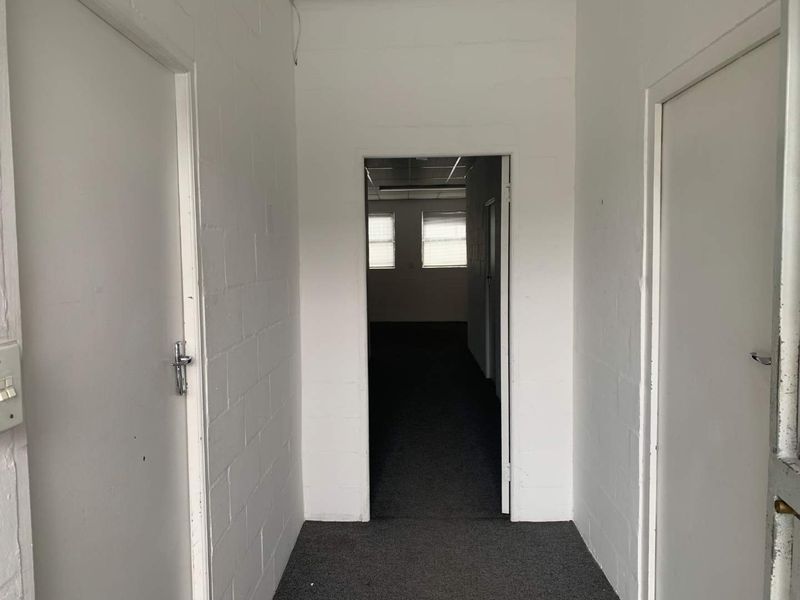 A functional, empty hallway featuring painted blockwork walls and carpeted flooring, providing access to adjacent rooms within the property.