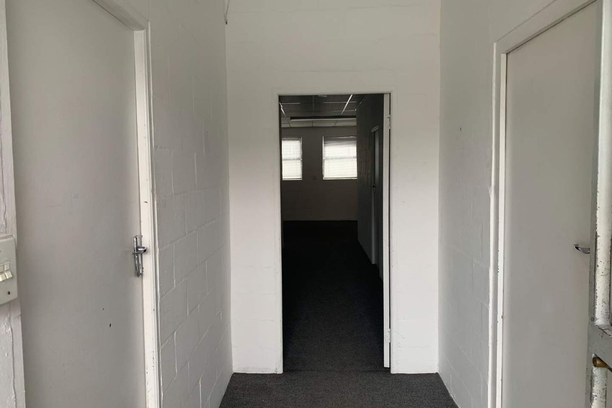 A functional, empty hallway featuring painted blockwork walls and carpeted flooring, providing access to adjacent rooms within the property.