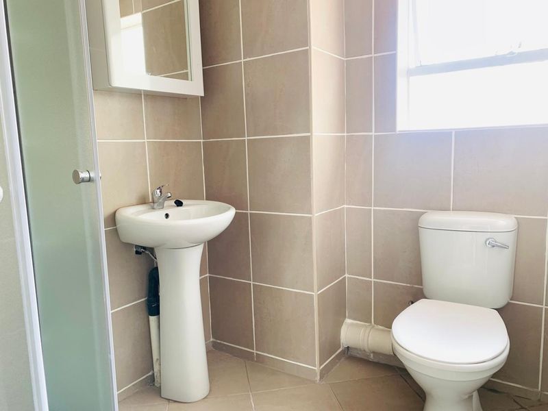 A functional bathroom featuring a pedestal basin, toilet, and shower enclosure with neutral wall and floor tiling.