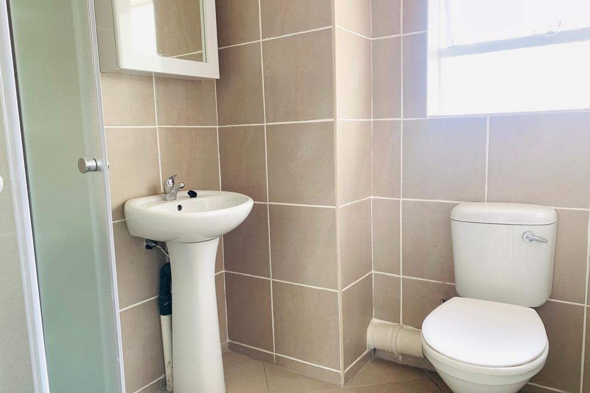 A functional bathroom featuring a pedestal basin, toilet, and shower enclosure with neutral wall and floor tiling.
