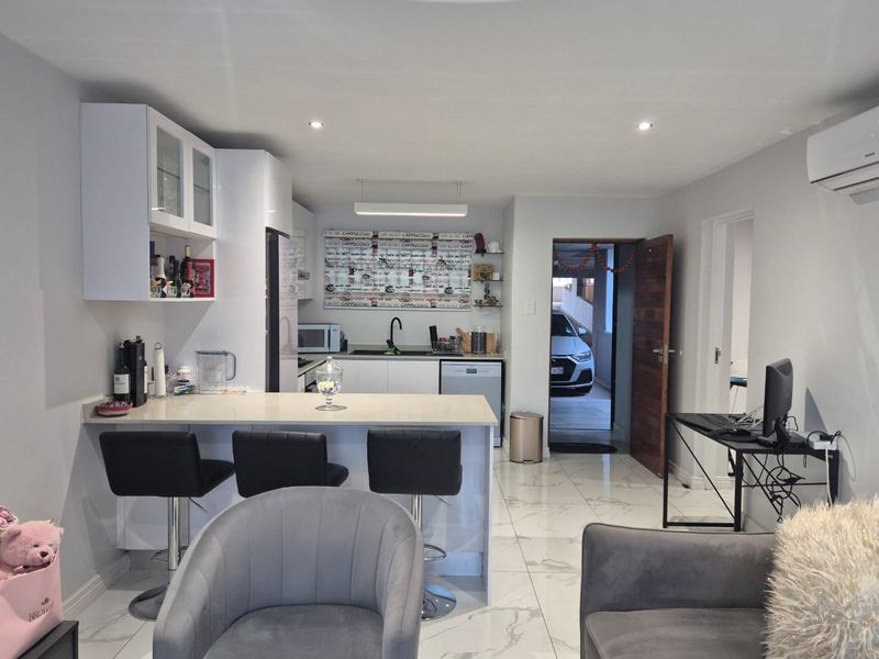 Modern open-plan kitchen and living area featuring sleek white cabinetry, quartz countertops, polished porcelain floor tiles, and integrated air conditioning.