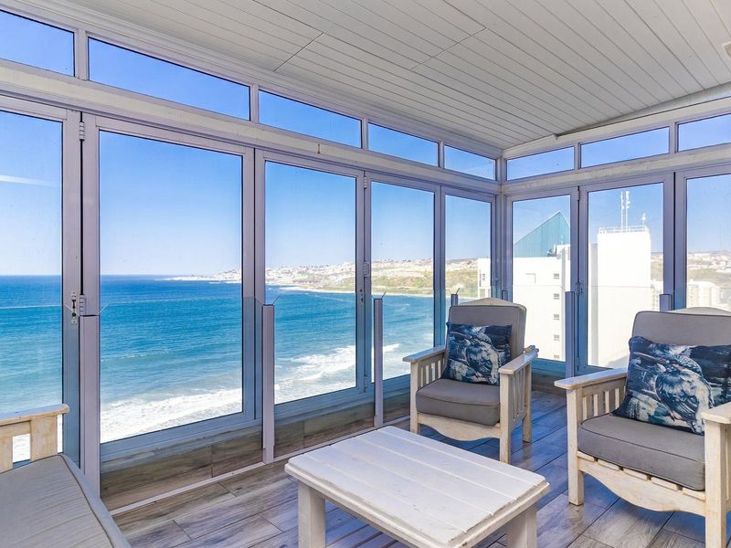 Enclosed balcony featuring floor-to-ceiling windows with panoramic ocean views, tiled flooring, and a built-in wood-burning fireplace.