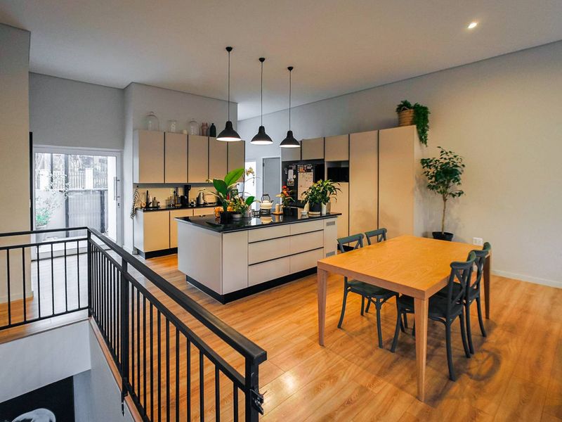 Modern open-plan kitchen and dining area featuring a central island, sleek cabinetry, warm wood-look flooring, and contemporary pendant lighting.