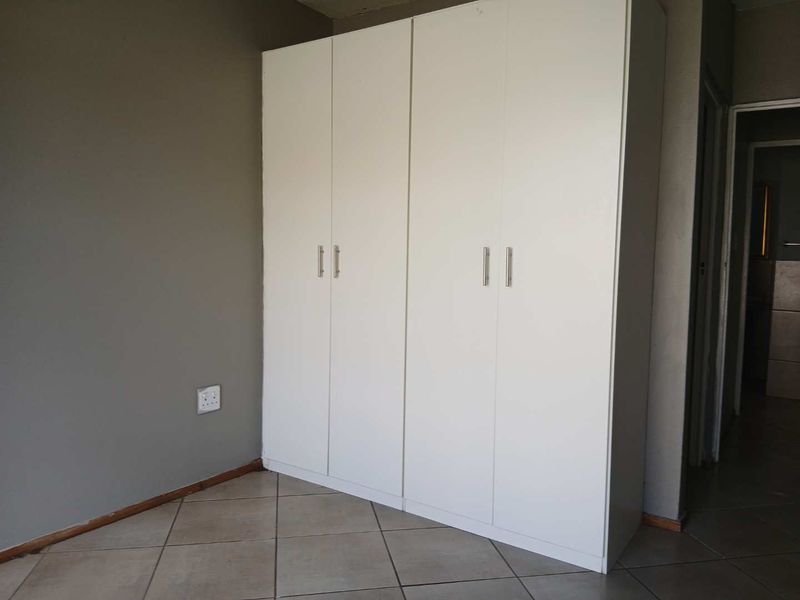 A bedroom featuring a white built-in wardrobe and neutral tiled flooring, offering a clean and functional space ready for personalization.